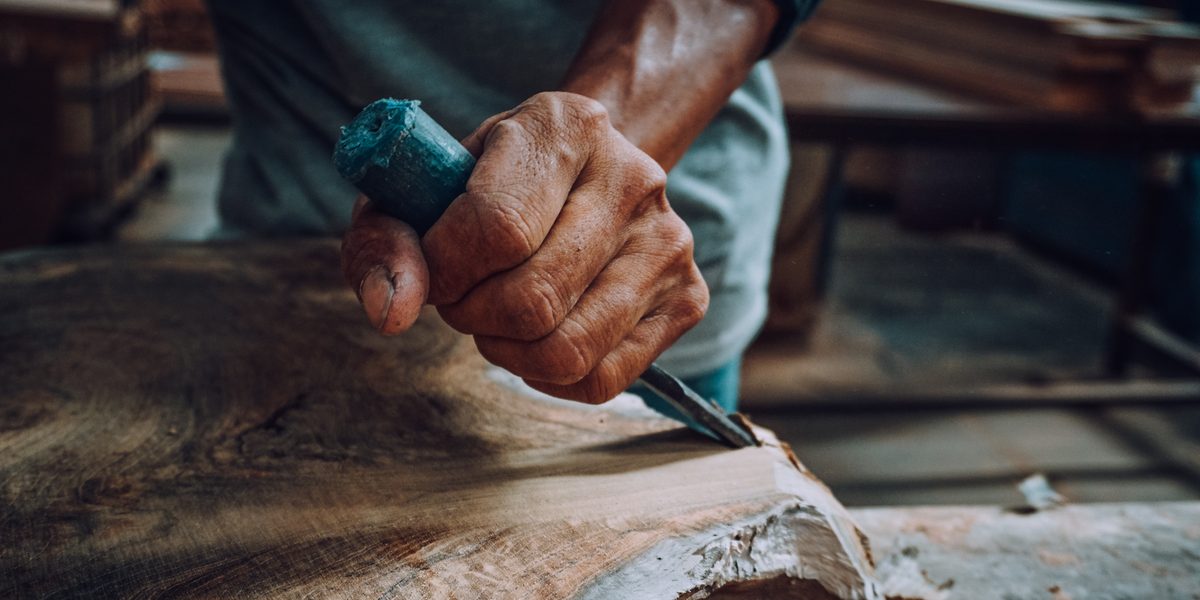 A Gamoora woodworker's hands carving the live edge of a slab with a chisel in the Java workshop