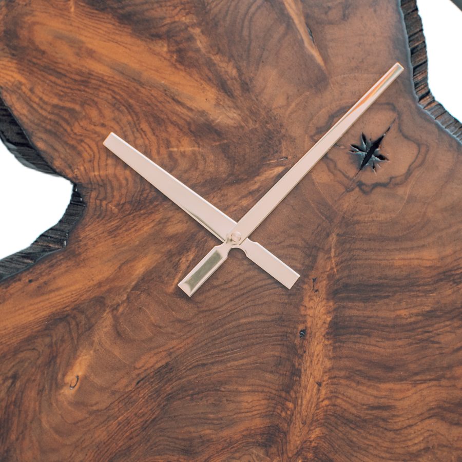 Close-up of a teak wall clock face showing swirling burl grain, natural voids and steel hands