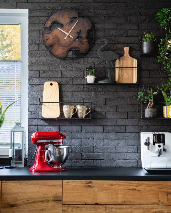 Teak wall clock on a black brick kitchen wall above a red stand mixer and coffee station
